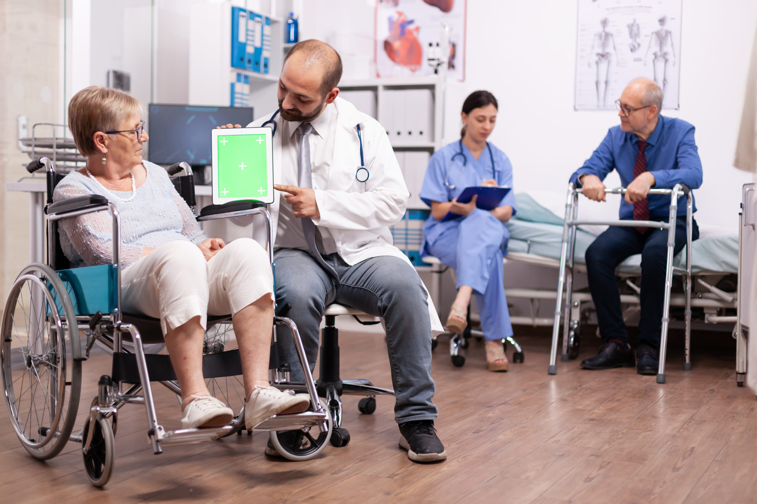 Therapist holding tablet pc with green screen in the course of therapy. Medical practitioner using device with chroma key during coonsultation of invalid senior woman.